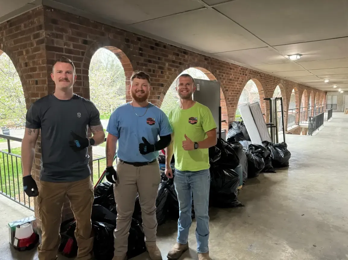 Three workers with trash bags outdoors.