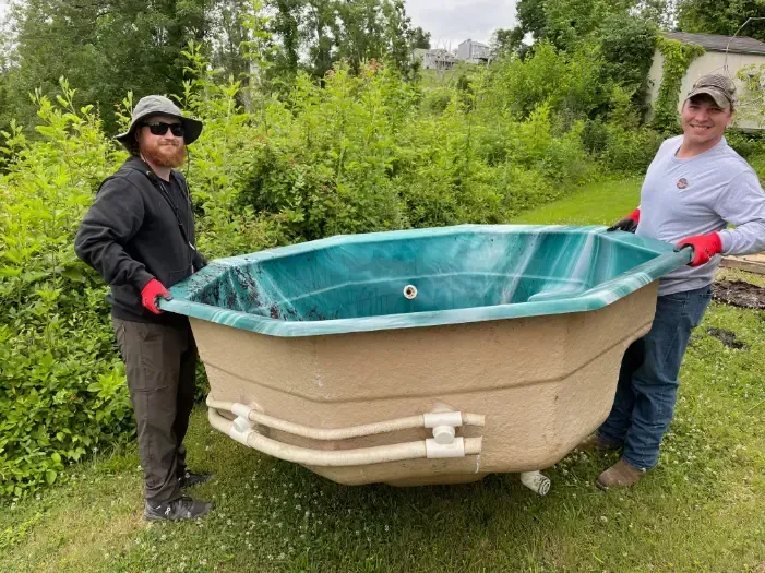 Two people carrying a hot tub.