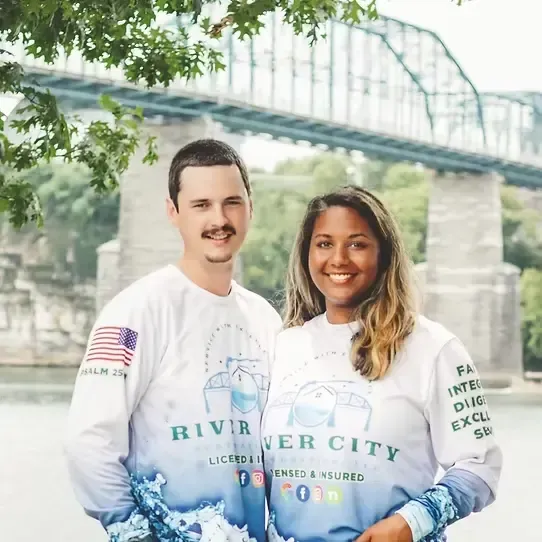 Couple by river with bridge backdrop.